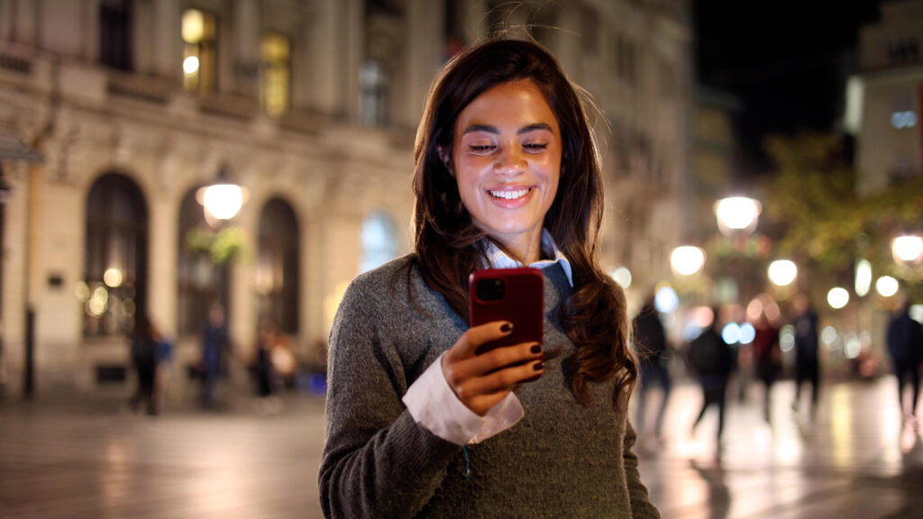 Mulher com celular, sorrindo e mandando mensagem para o crush